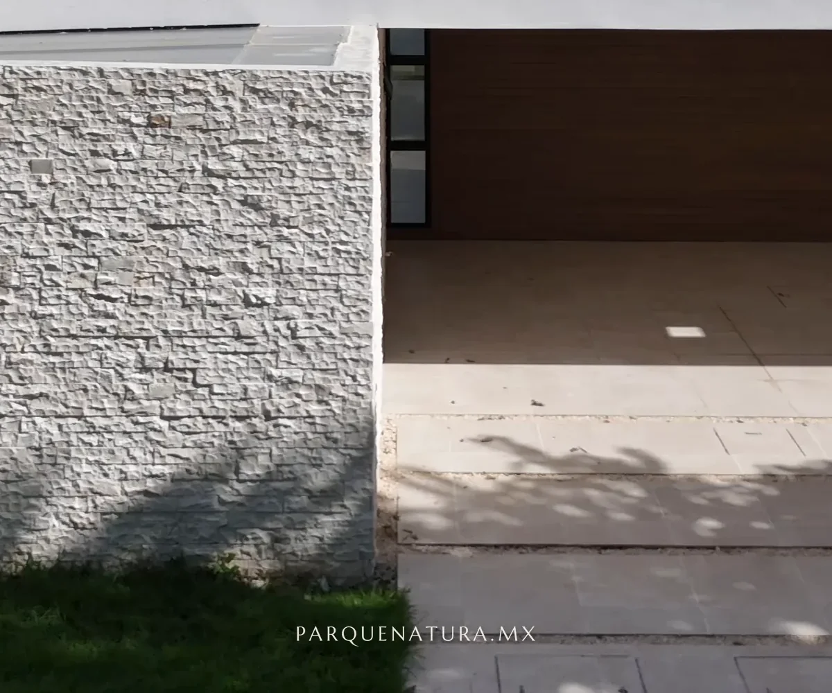 Fachada de la Casa 208 de Parque Natura I: muro de piedra, cochera techada y pasto